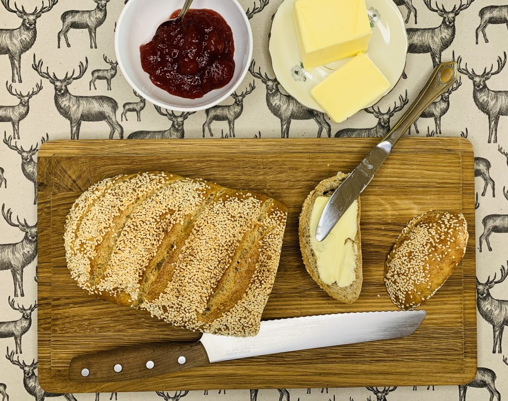 Friskbagt brød med sesam, skåret på et bræt med smør og marmelade