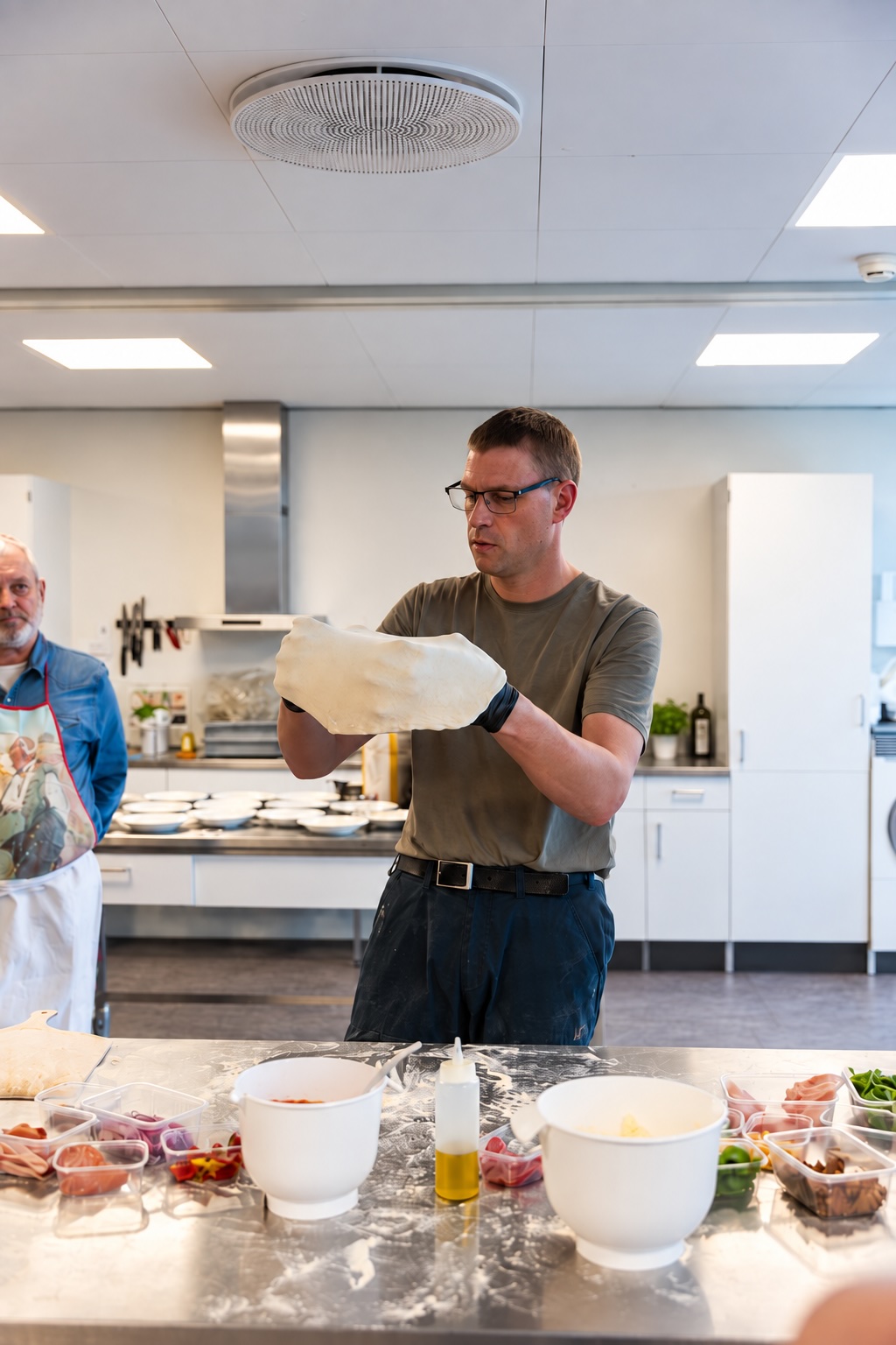 Underviser demonstrerer udstrakt pizzadej på pizzakursus